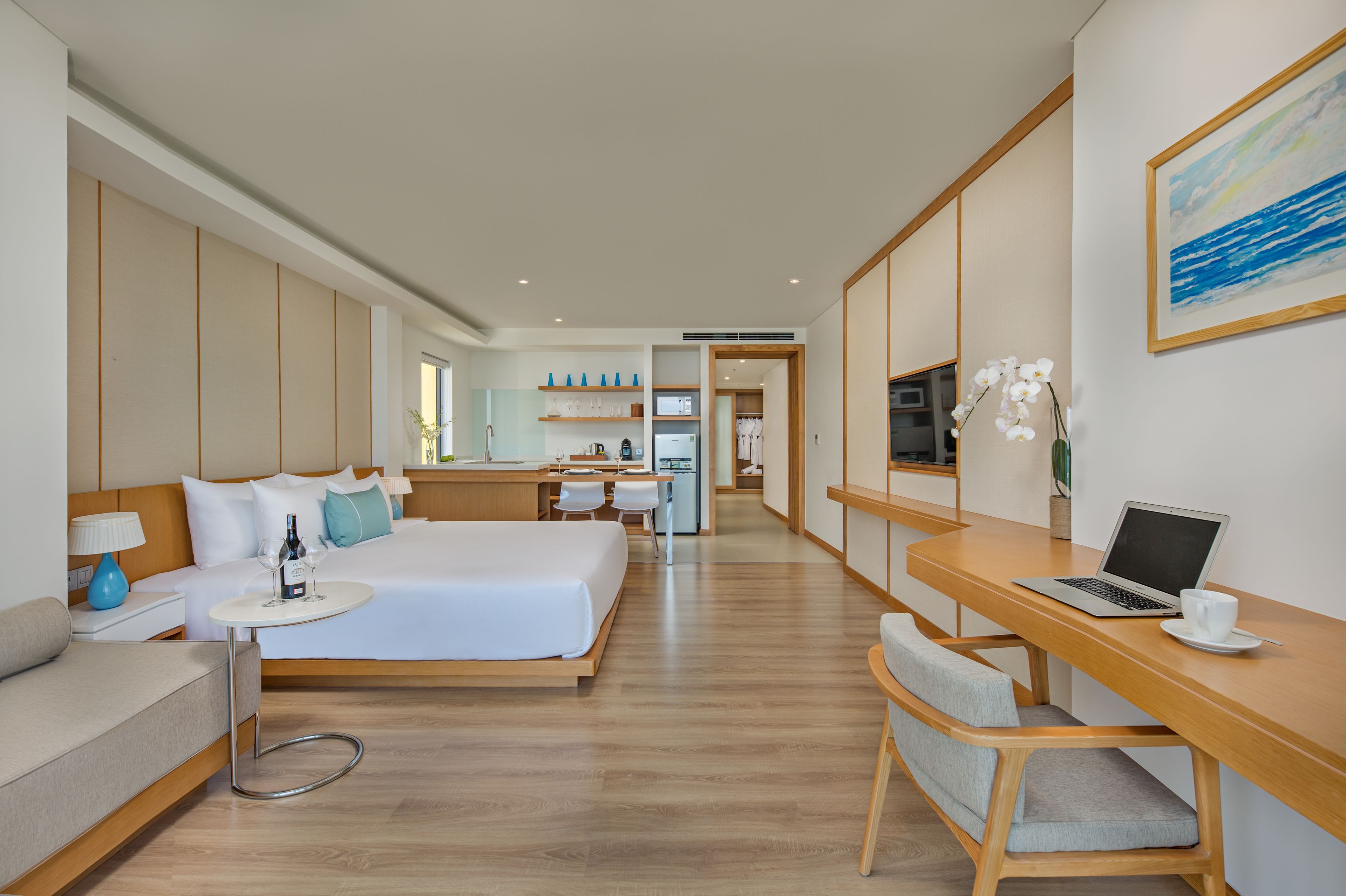Una habitación de hotel moderna con una cama grande, un escritorio con una computadora portátil, un sofá y una zona de comedor.