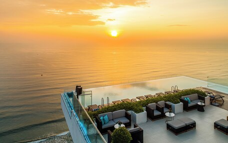 A rooftop lounge with a pool, outdoor seating, and a view of the sunset over the ocean.