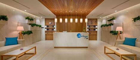 A reception area with a reception desk, two sofas, a coffee table, and shelves with plants and items.