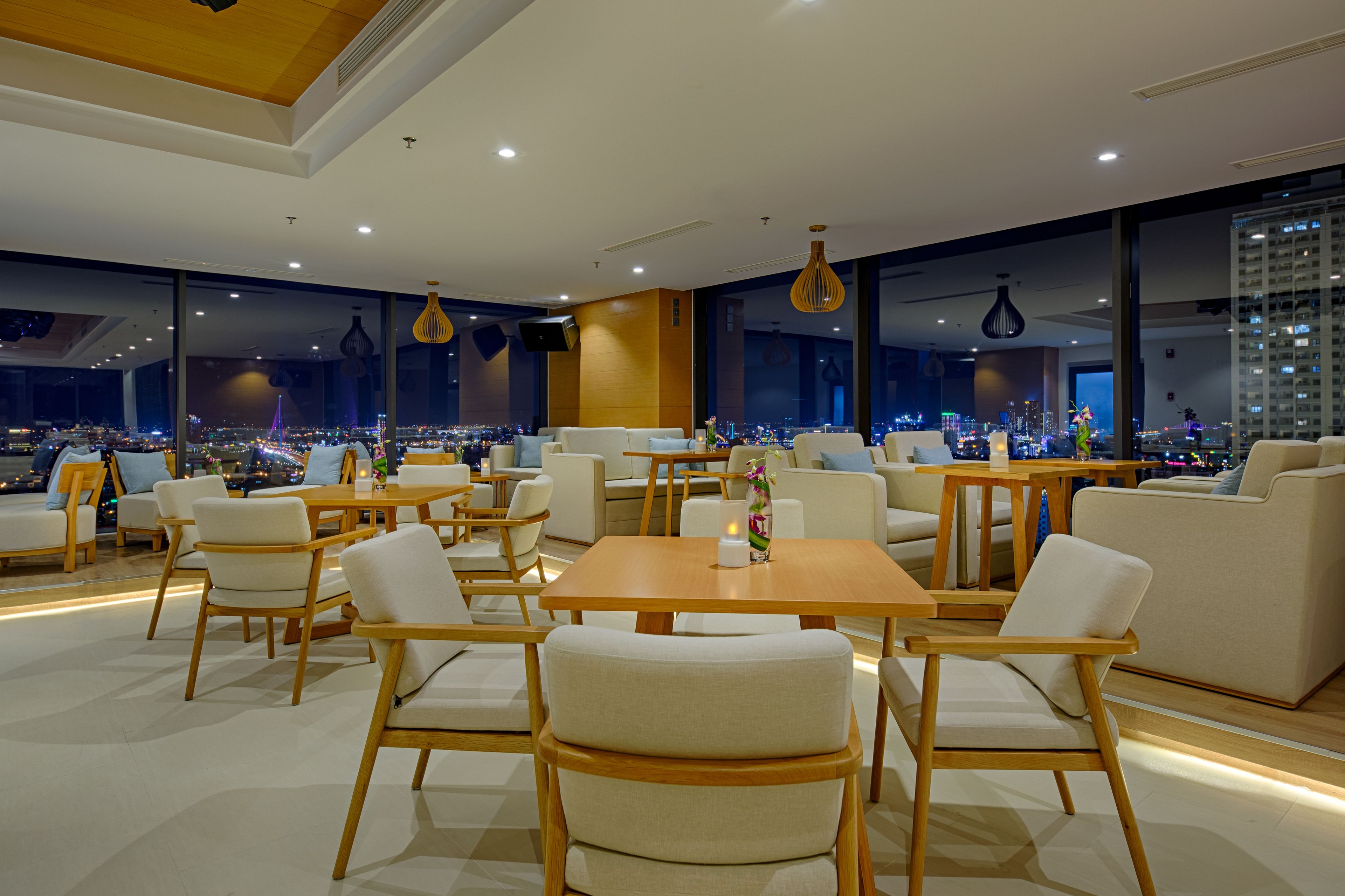 Ein modernes Restaurant mit Blick auf die Stadt, ausgestattet mit Holztischen und -stühlen sowie großen Fenstern.