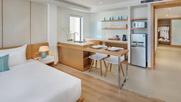 A modern hotel room with a large bed, a small kitchenette, and a separate dining area.