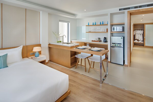 A modern hotel room with a large bed, a small kitchenette, and a separate dining area.