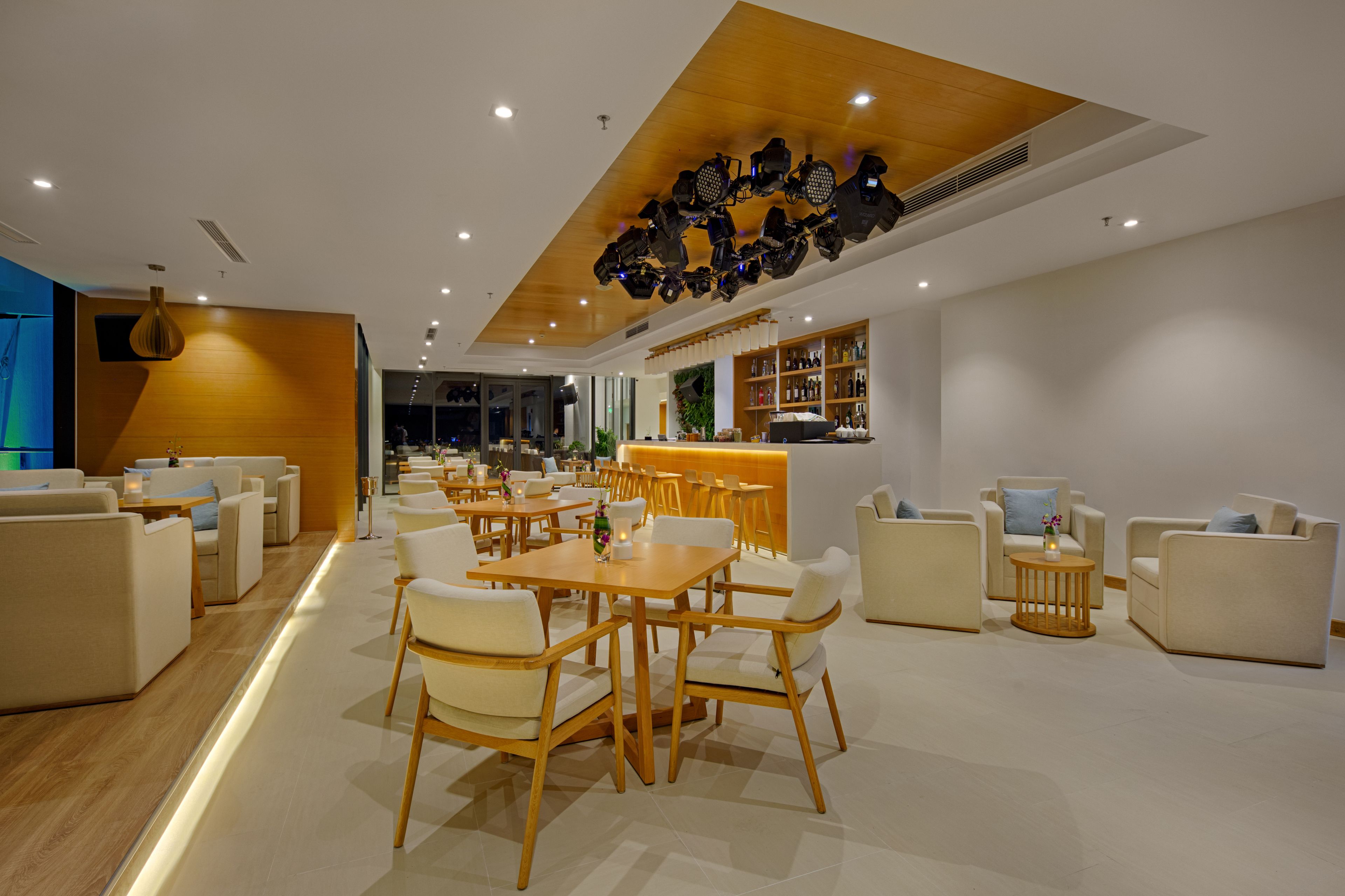 A modern hotel lobby with a wooden ceiling, white sofas, and a bar area.