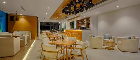 Un hall d’hôtel moderne avec un plafond en bois, des canapés blancs et un espace bar.