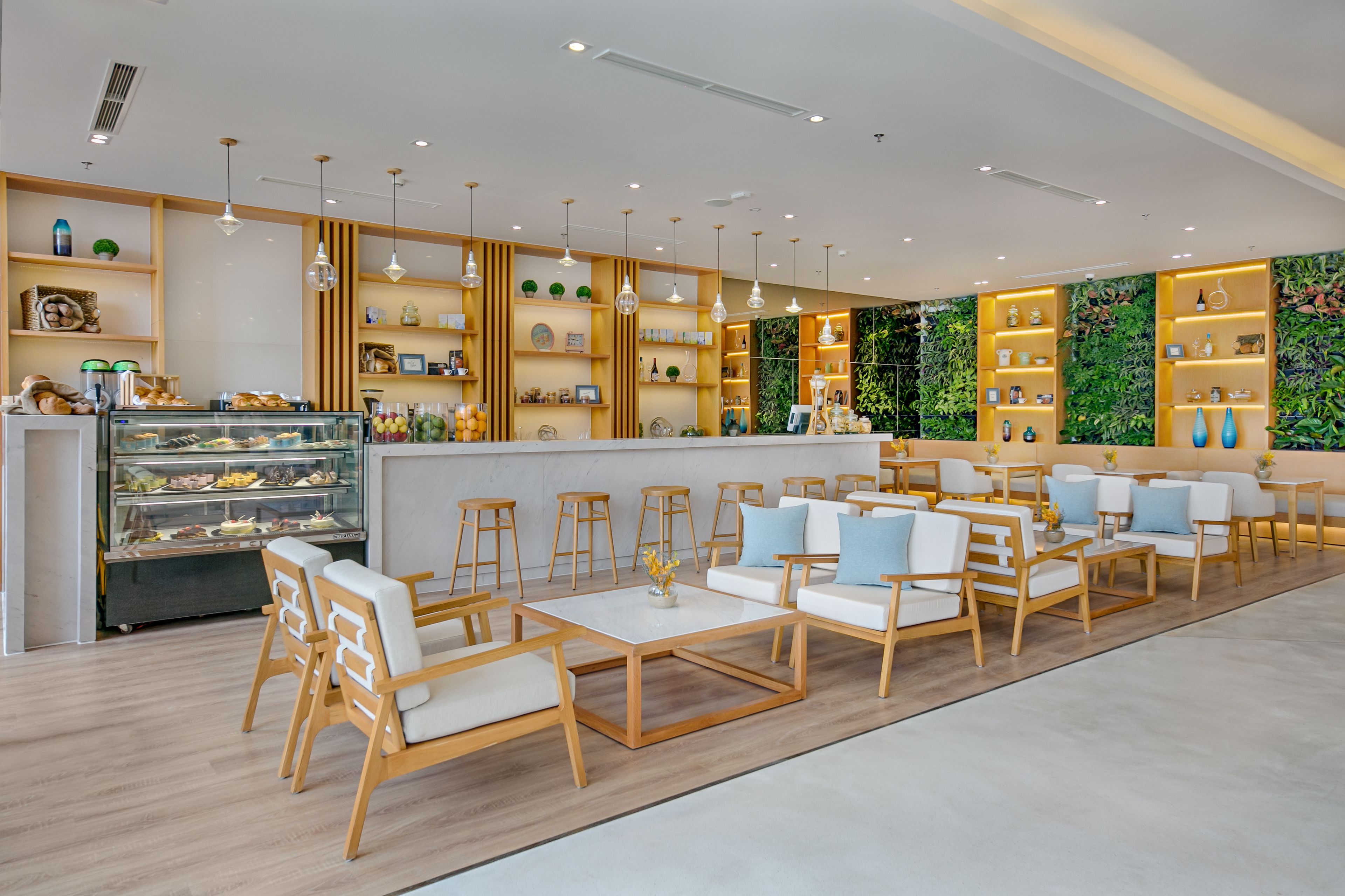 Um café moderno com móveis de madeira, uma vitrine com doces e estantes com objetos decorativos.
