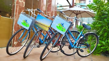 Three bicycles with baskets, each with a different advertisement, parked in an indoor area with a marble wall and greenery in the background.
