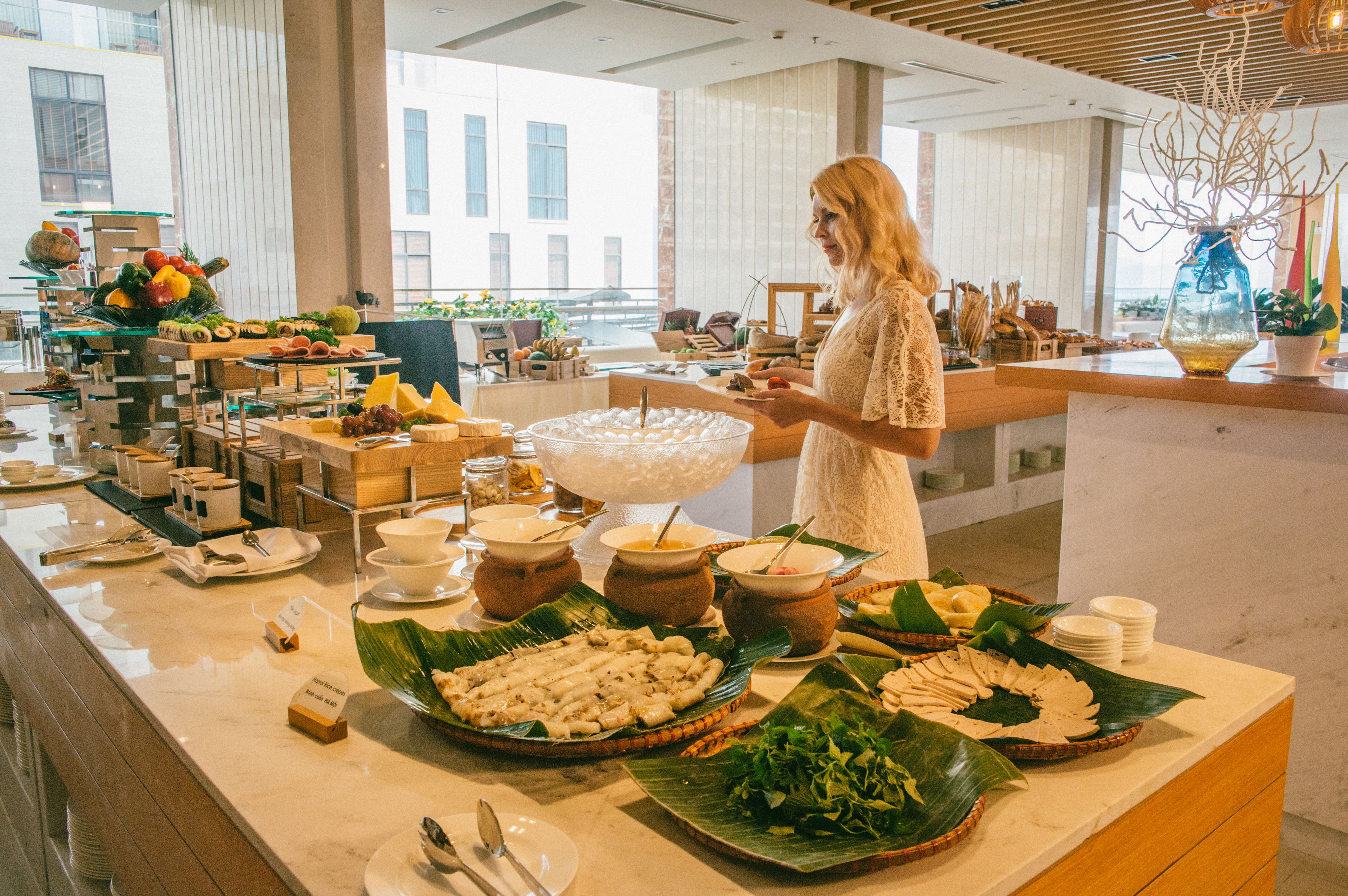 A buffet setup with various food items and a woman serving.