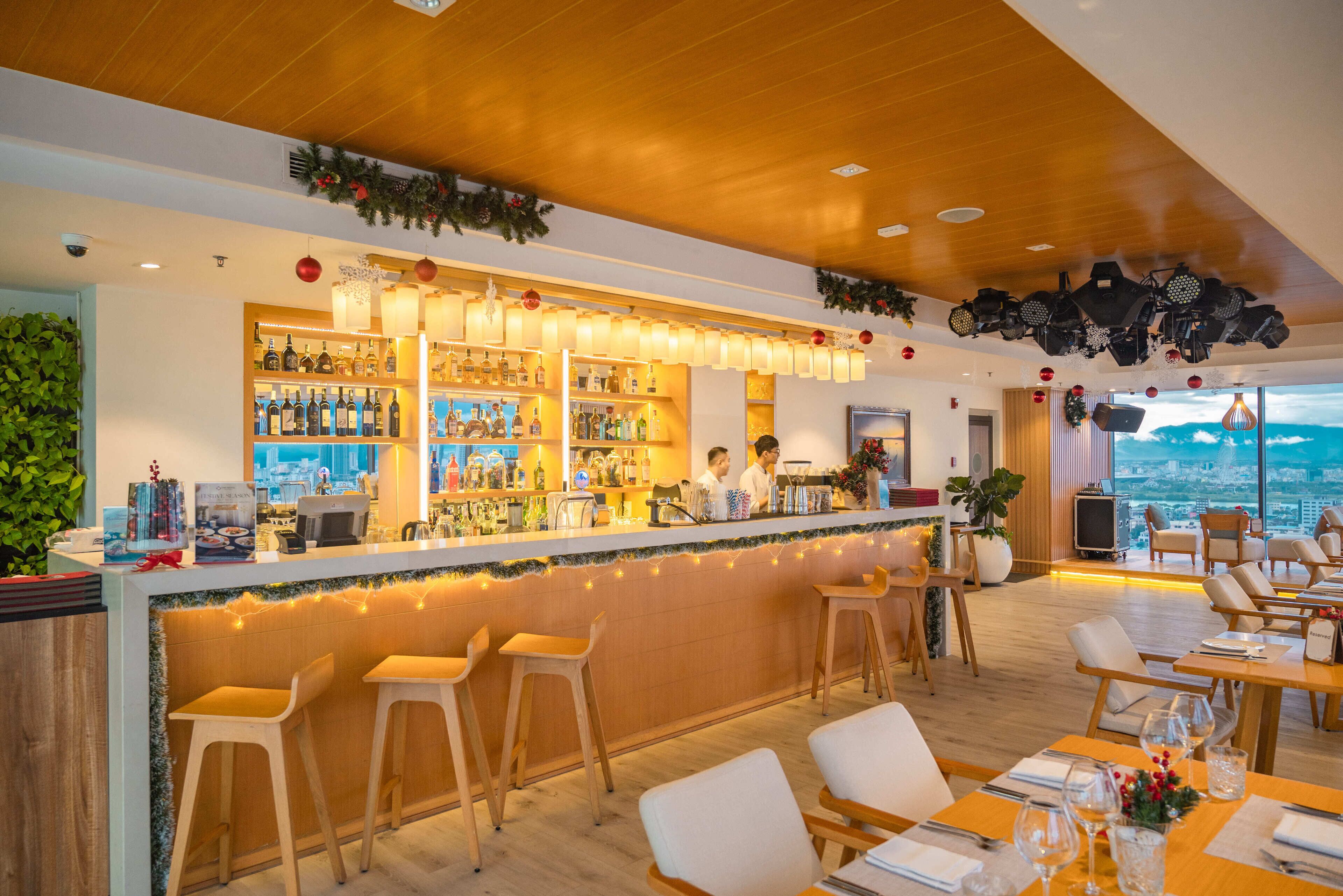 Uma área de bar com balcão de madeira, banquetas e vista da cidade.