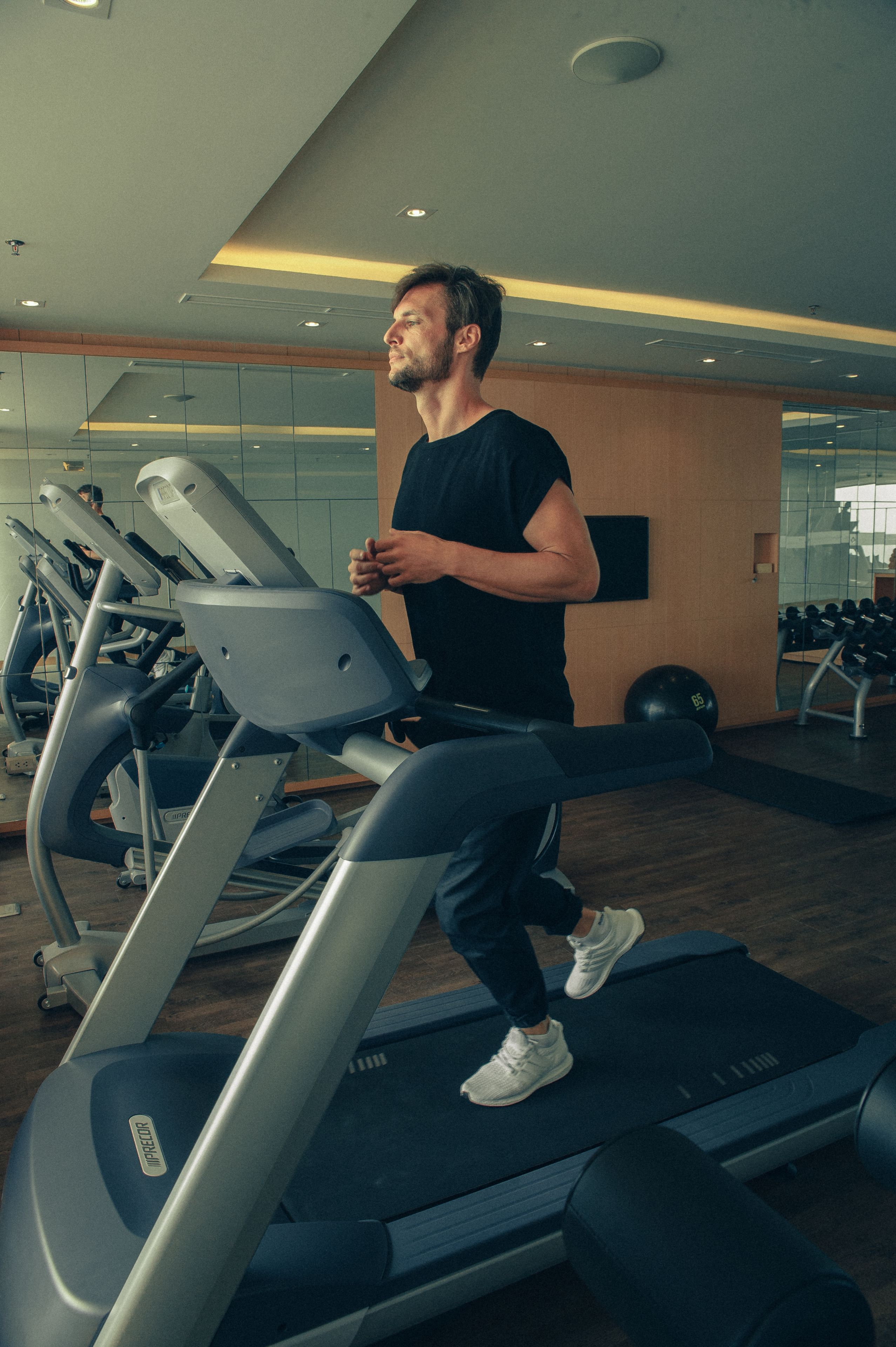 A man running on a treadmill in a gym with exercise equipment and a mirror on the wall.