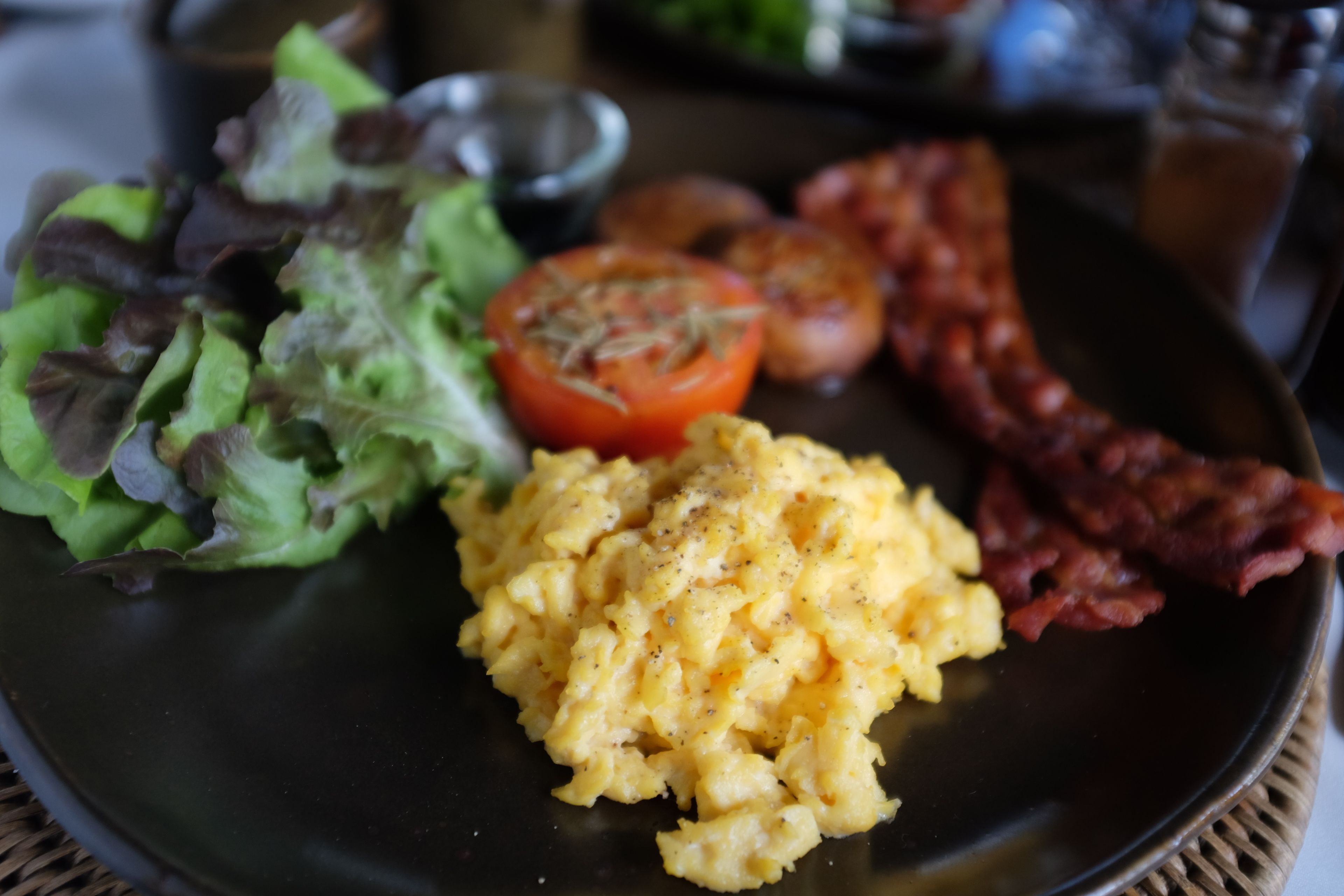 A plate with scrambled eggs, bacon, a tomato, and a side salad.