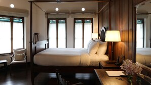 A hotel room with a large bed, a desk with a lamp, a chair, and a small table.