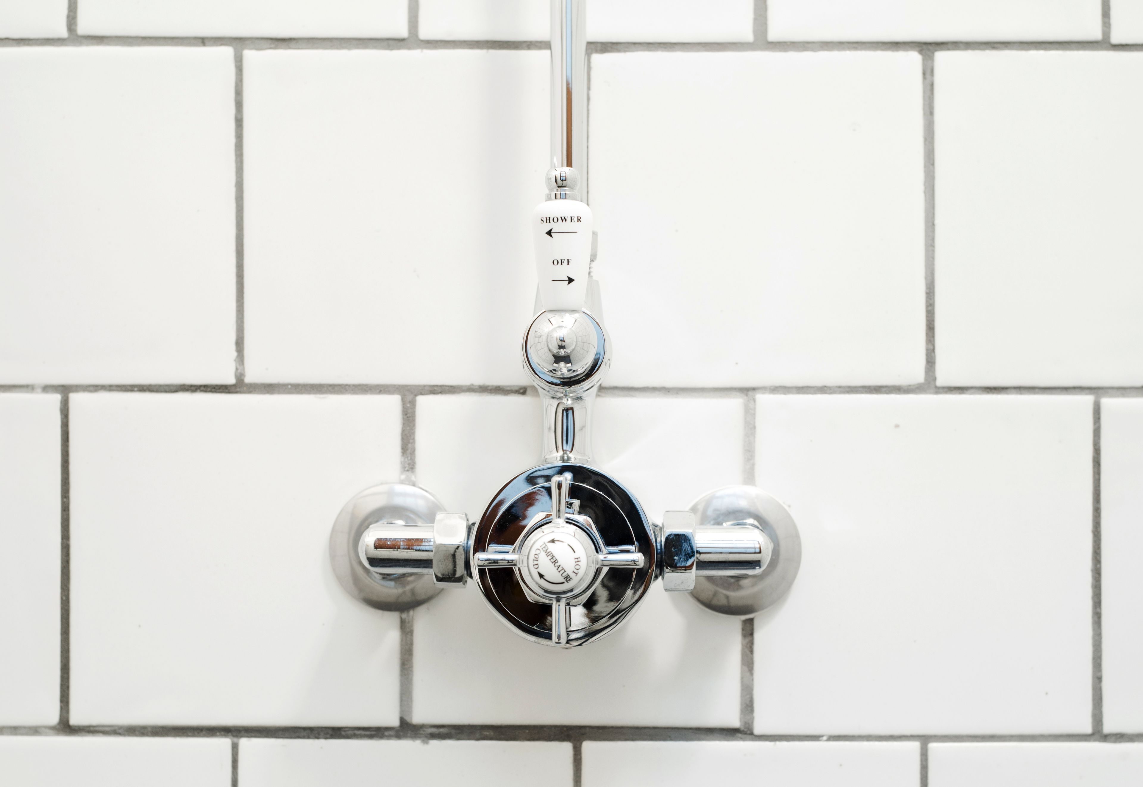 A shower control valve mounted on a white tiled wall.