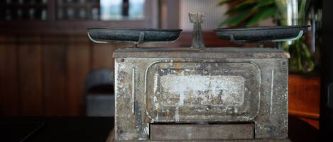 An old-fashioned scale with a wooden base, set against a blurred background with a plant and a window.
