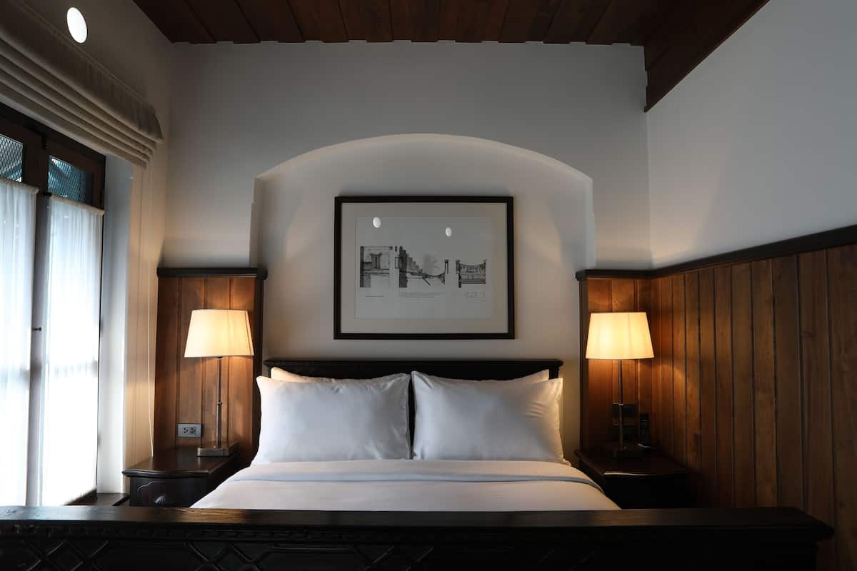 A hotel room with a large bed, two bedside lamps, a framed picture on the wall, and wooden paneling on the walls.