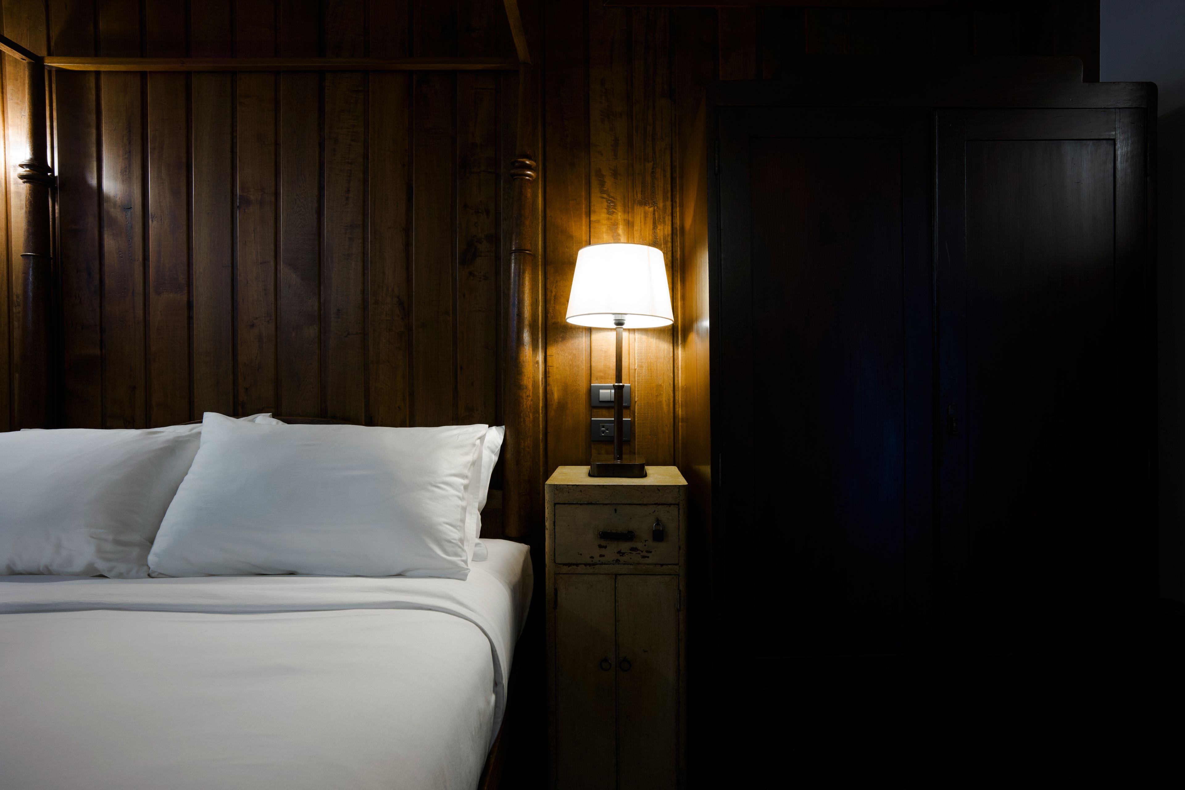 Ein Zimmer mit Holzwänden, einem Bett, einem Nachttisch mit Lampe und einem Kleiderschrank.