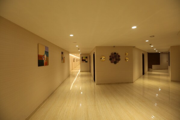 A long, well-lit hallway with a polished floor, artwork on the walls, and a decorative wall piece. - M Crown Hotel (Shillong)