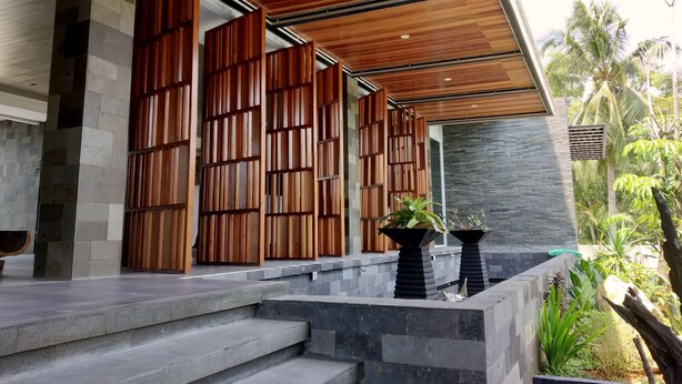 A modern outdoor entrance with wooden slats, stone steps, and a view of tropical vegetation. - Quins Style Resort Belitung (Tanjung Pandan)