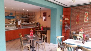 Um restaurante com balcão, mesas, cadeiras e um ventilador.