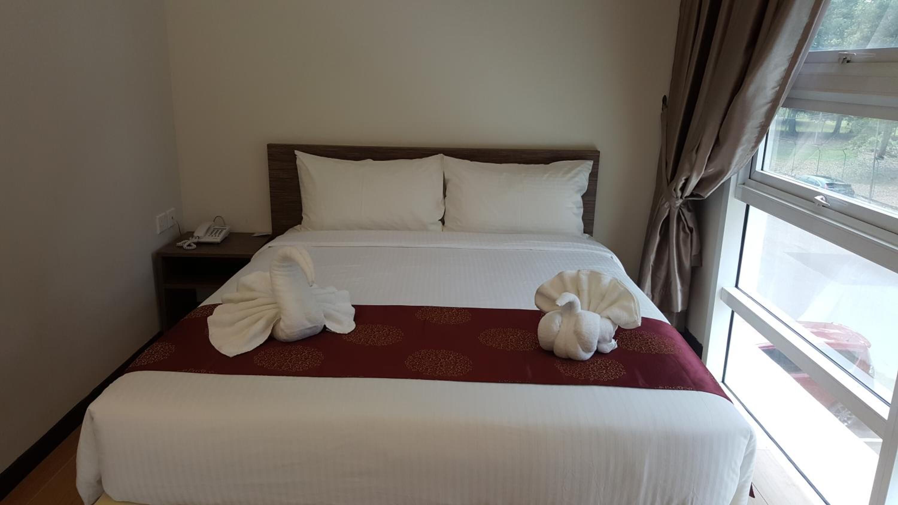 Una habitación de hotel con una cama bien hecha, un teléfono en la mesita de noche y una ventana con cortinas.