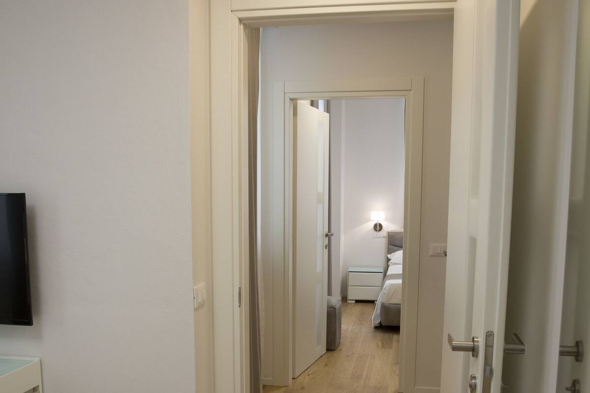 A hallway with wooden flooring, white walls, and a television mounted on the left.