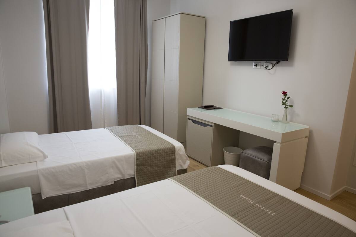 A hotel room with two beds, a desk, a television, and a small trash bin.