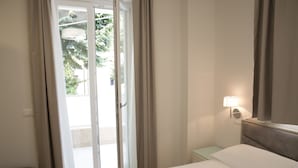 Habitación de hotel con cama, mesita de noche, lámpara y puerta corrediza de vidrio que da a un área exterior.