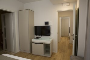 A compact room with a TV on a white cabinet, a small glass table, and a door leading to another room. - Boutique Hotel Enia (Prato)