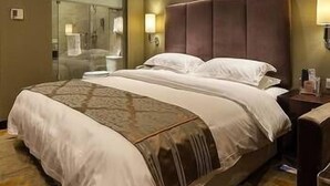 A hotel room with a large bed, a nightstand, a lamp, and a mirror. - Xinchuan Shouzuo Hotel (Mianyang)