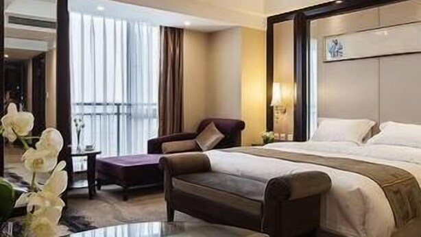 A hotel room with a large bed, a sofa, a small table with a cup and saucer, and a view of the outdoors. - Xinchuan Shouzuo Hotel (Mianyang)