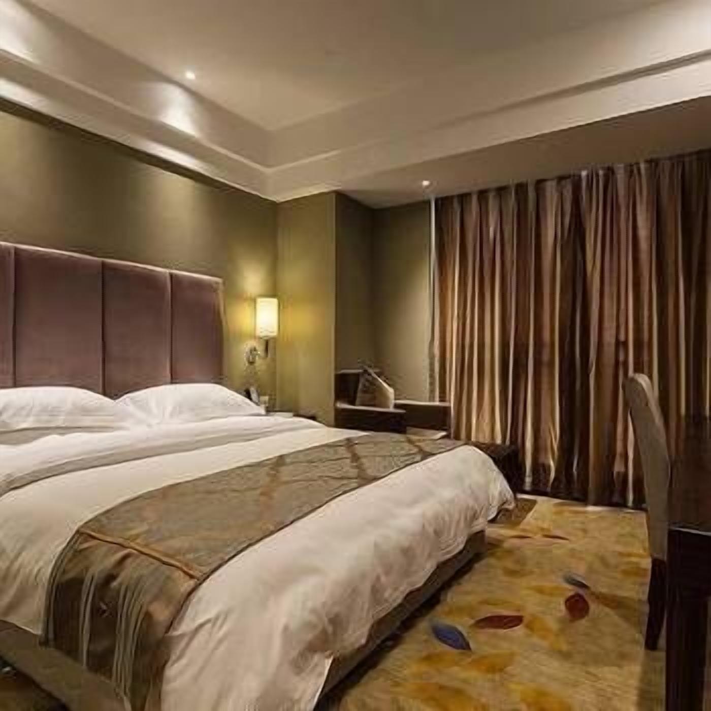 Une chambre d’hôtel avec un grand lit, une table de chevet, une lampe et une vue sur l’extérieur à travers les rideaux.