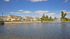A row of waterfront condominiums with a fountain and trees in the background. - Ec21ha - 3 Bedroom Townhome In Villas at Seven Dwarfs Lane, Sleeps Up To 6, Just 6 Miles To Disney (Kissimmee)