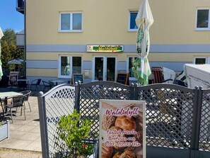 An outdoor seating area with tables and chairs, a sign for 'Waldidyll' bakery, and a lattice fence. - Ferienwohnung Zweisamkeit (Gelbensande)