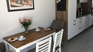 A small dining area with a wooden table, white chairs, a vase of flowers, and a framed painting on the wall. - Ferienwohnung Zweisamkeit (Gelbensande)