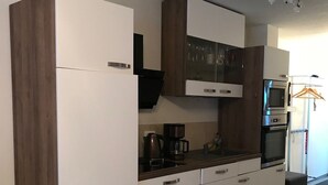 A modern kitchen with white cabinets, a built-in oven, and a coffee maker. - Ferienwohnung Zweisamkeit (Gelbensande)