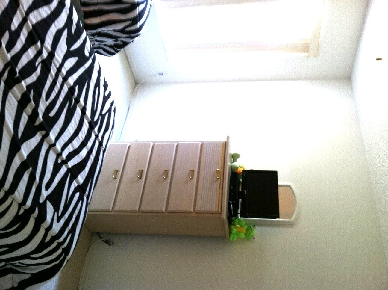 Una habitación con una pared blanca, un mueble beige con cuatro cajones y un objeto negro pequeño encima.