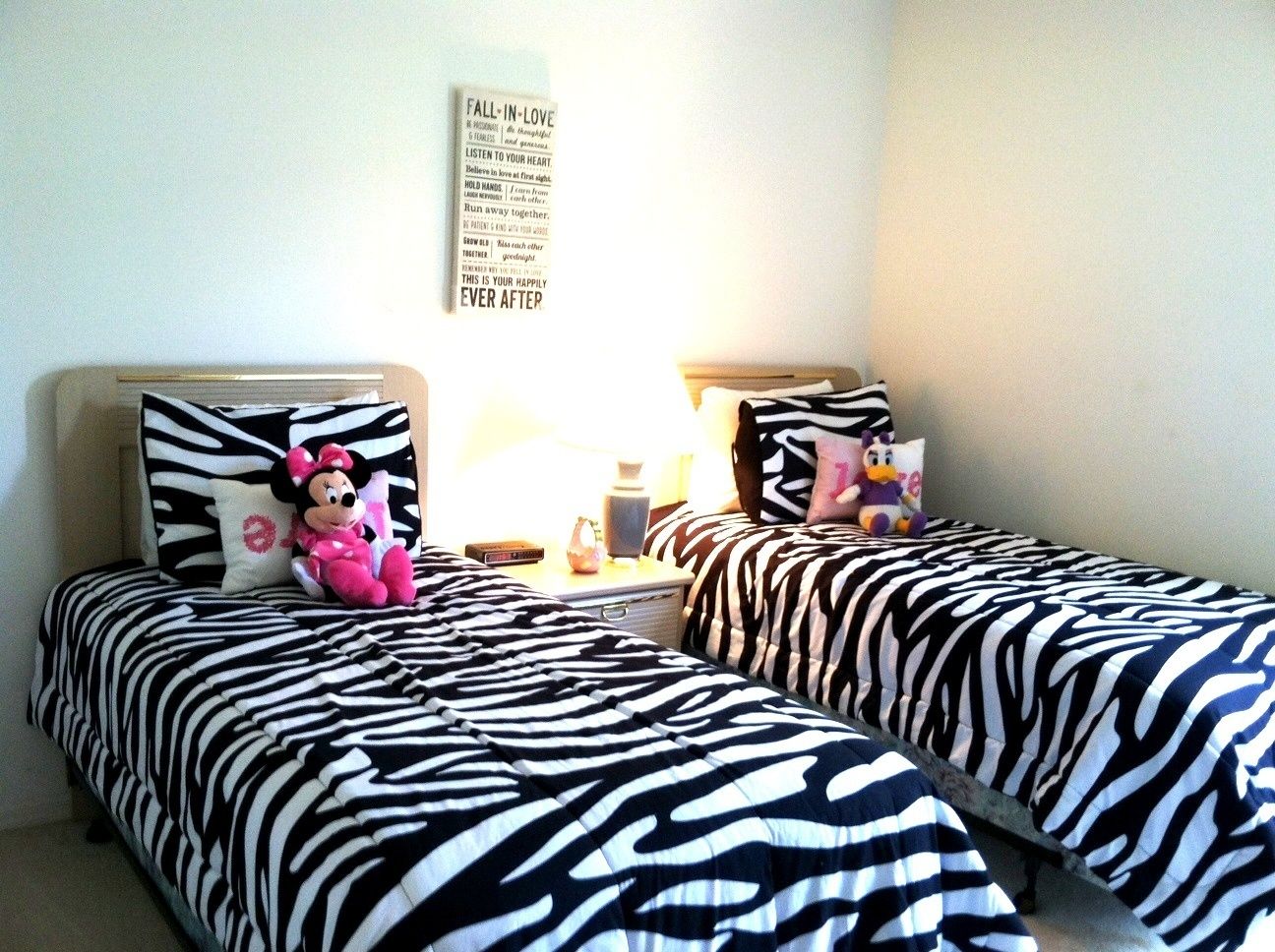 A bedroom with two beds, zebra-patterned bedding, a wall with motivational quotes, and a Minnie Mouse plush toy on one bed.