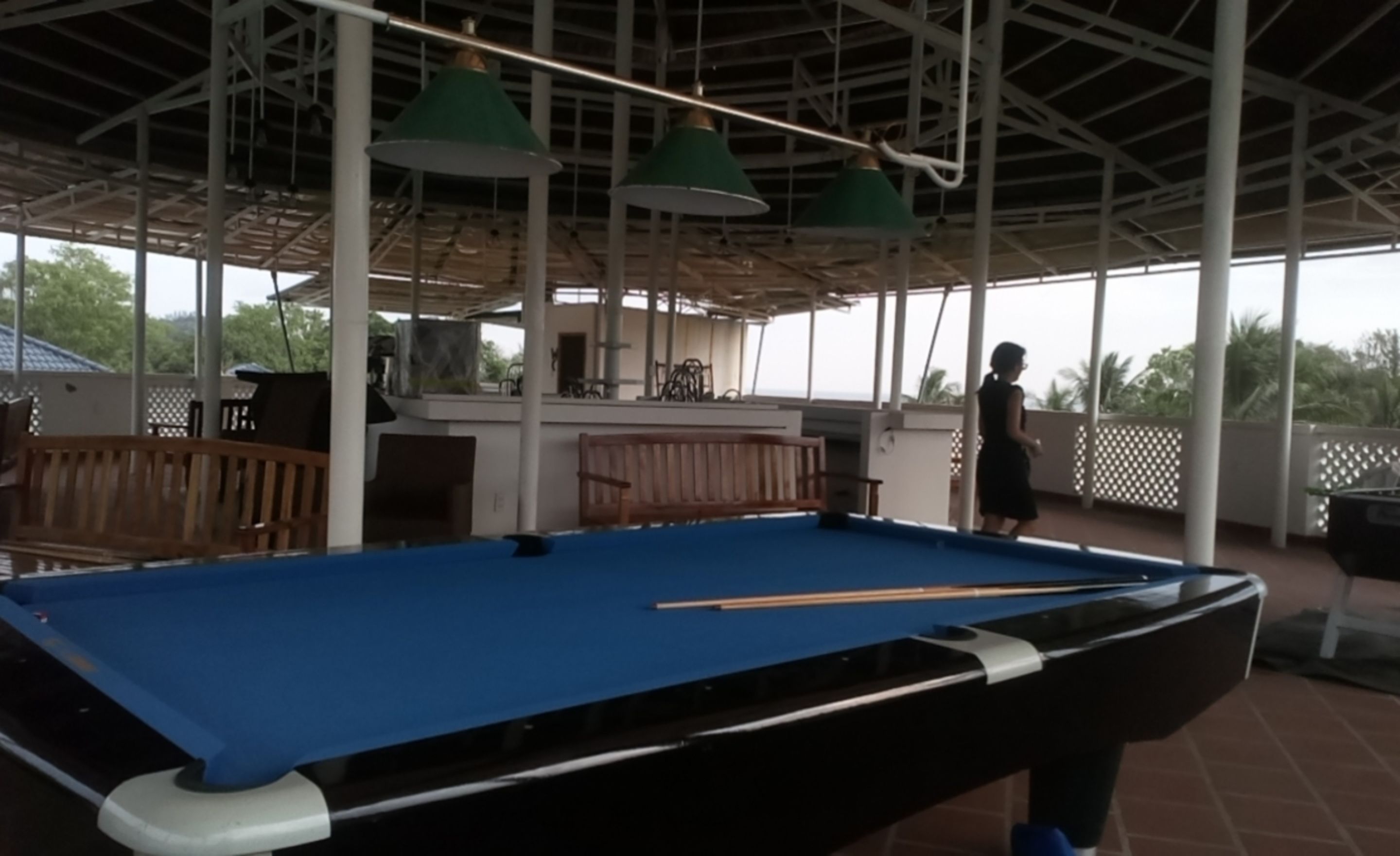 Une table de billard installée dans un espace extérieur doté d’un toit abrité, de bancs et de lampes suspendues.