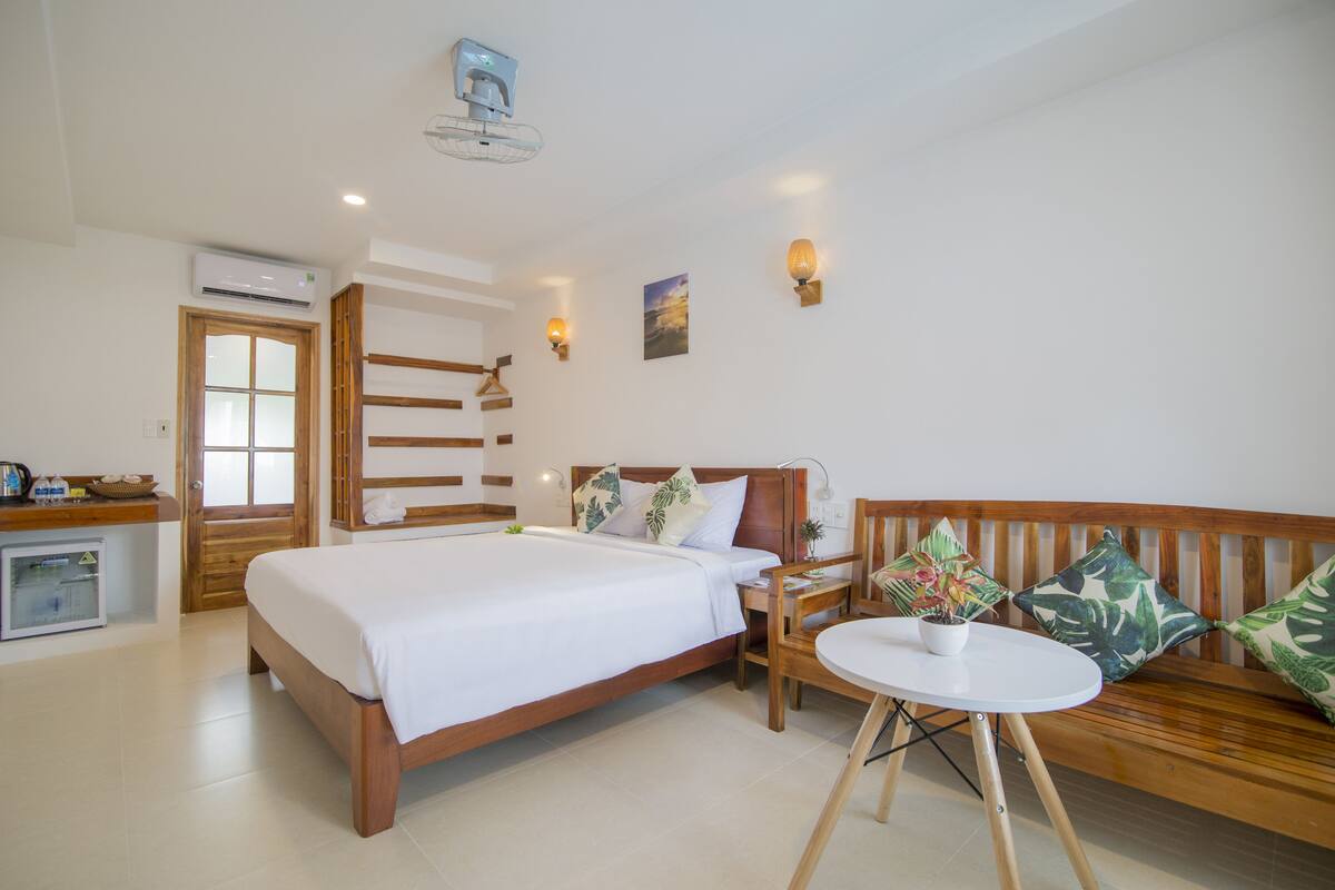 Une chambre d’hôtel avec un lit, une petite table, un banc et un climatiseur fixé au mur.