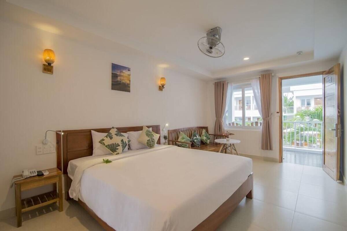 Une chambre d’hôtel avec un grand lit, des tables de chevet, une petite table, un ventilateur de plafond et une vue sur l’extérieur.
