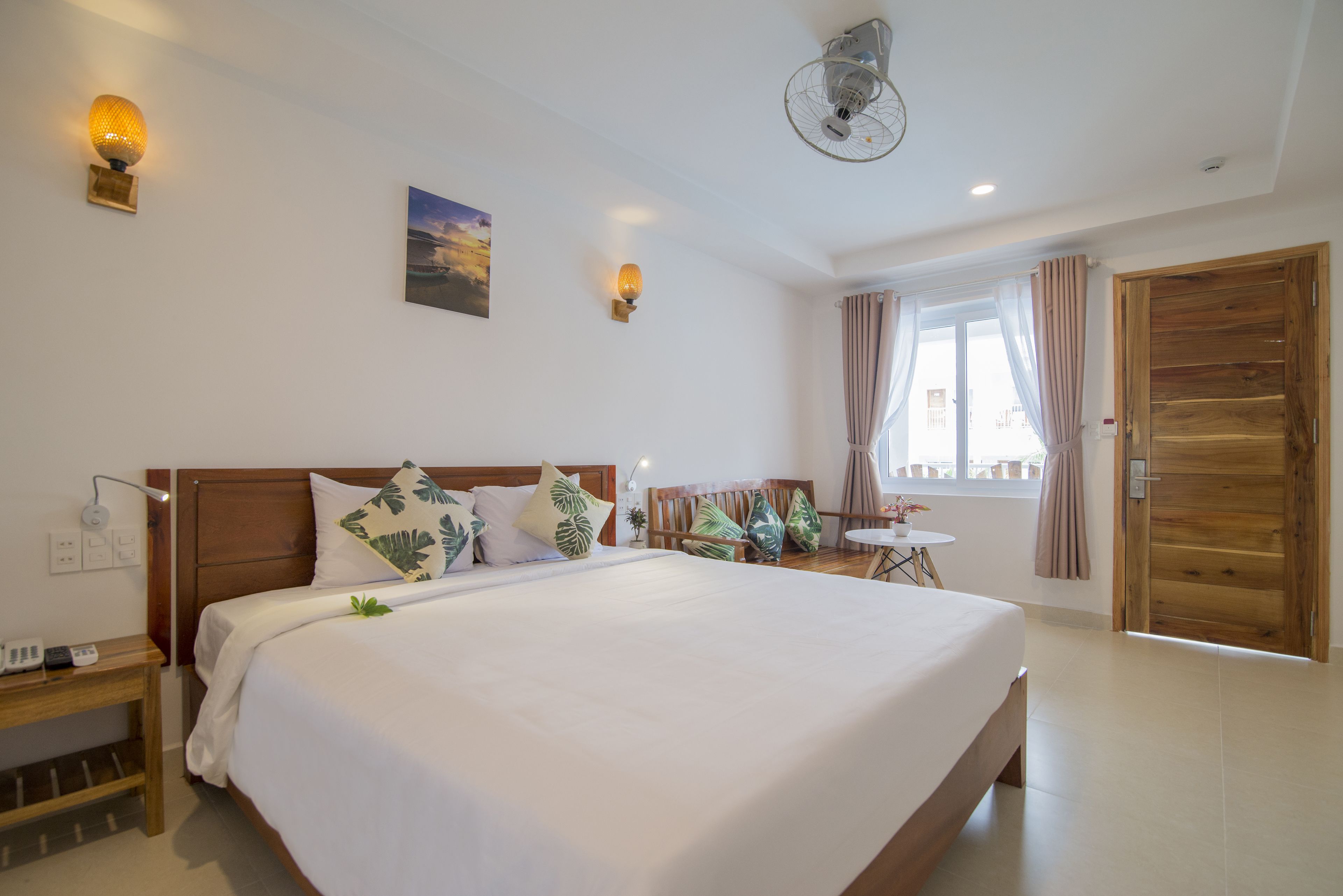 A spacious bedroom with a large bed, a wooden headboard, a bedside table, and a small table with chairs.