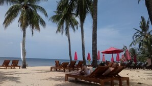 A beach with wooden lounge chairs and red umbrellas. - Palma Resort Phu Quoc, Trademark Collection by Wyndham (Phu Quoc)