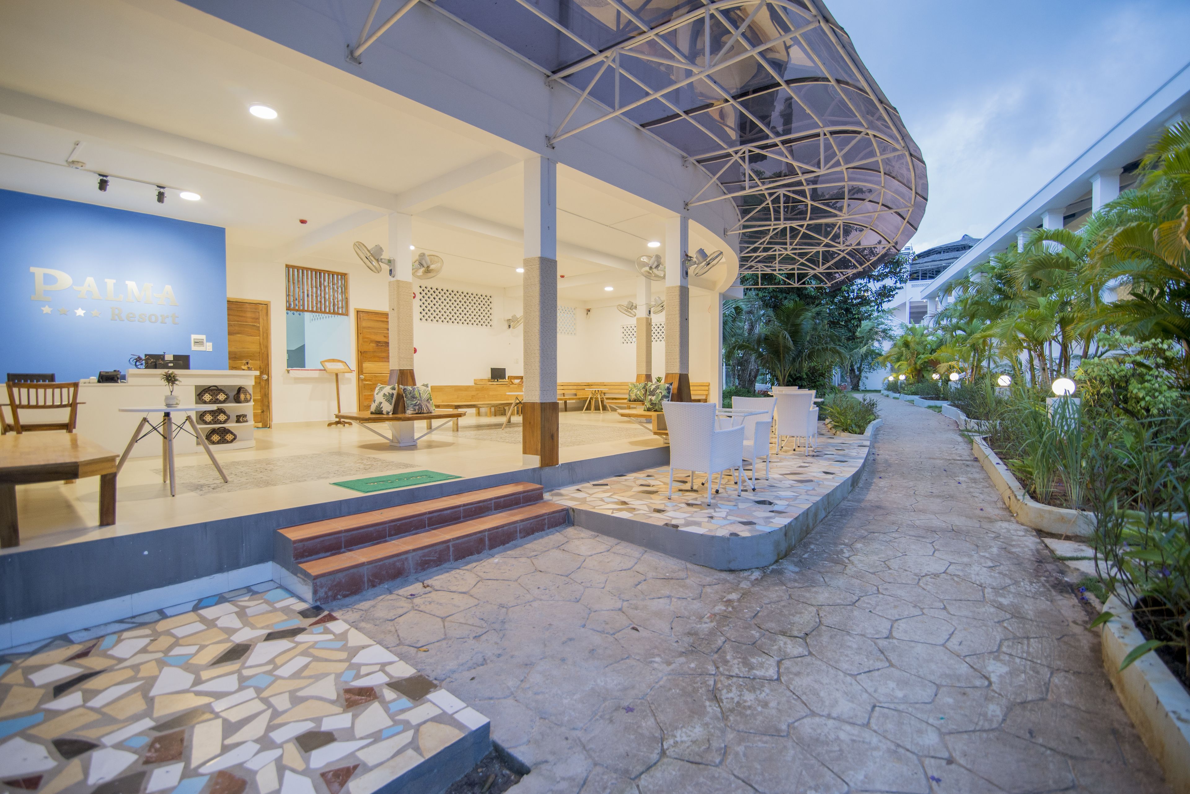 A hotel entrance with a reception desk, seating area, and a covered outdoor space with steps leading to the entrance.