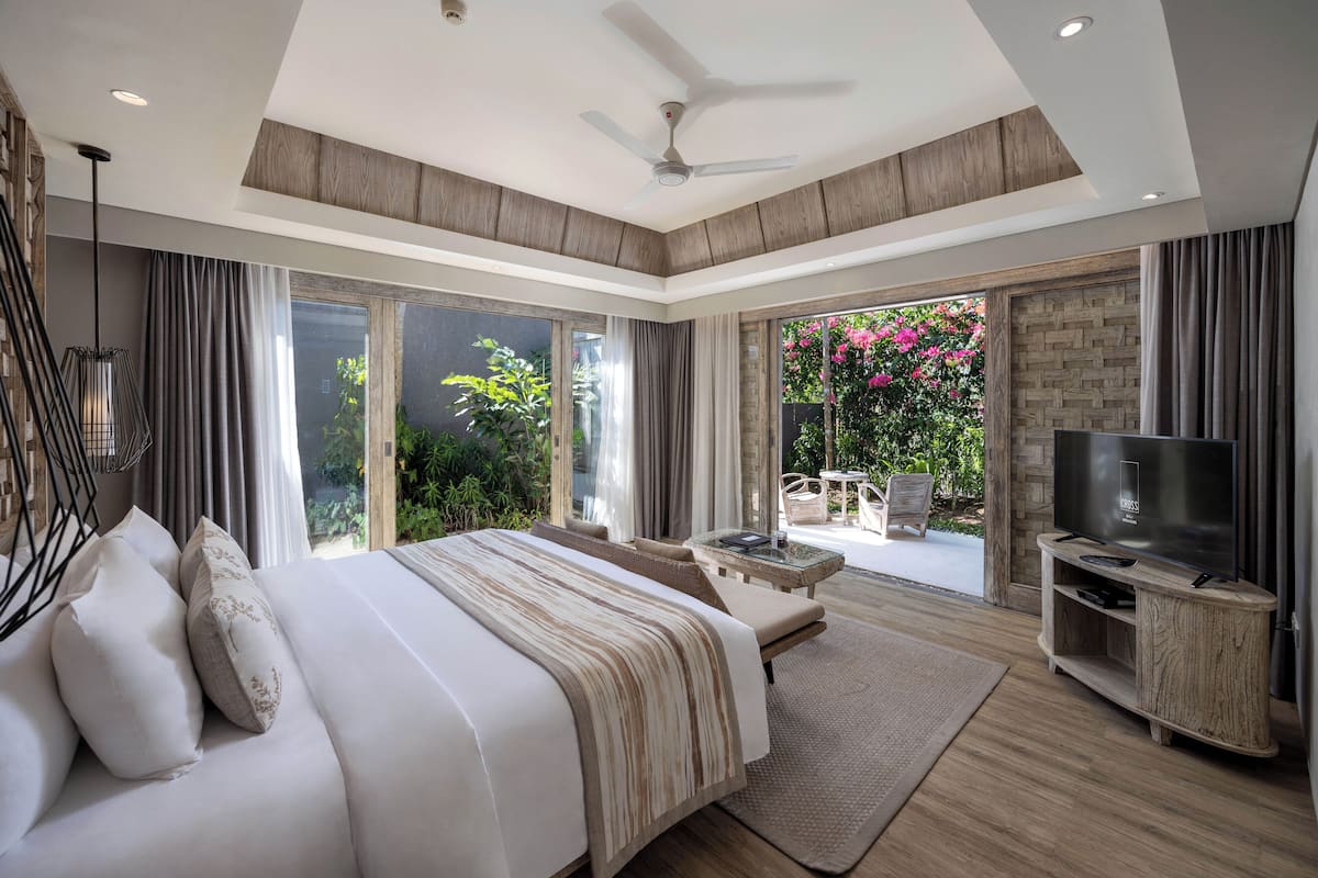 A spacious bedroom with a large bed, a TV, and a balcony with a view of greenery.