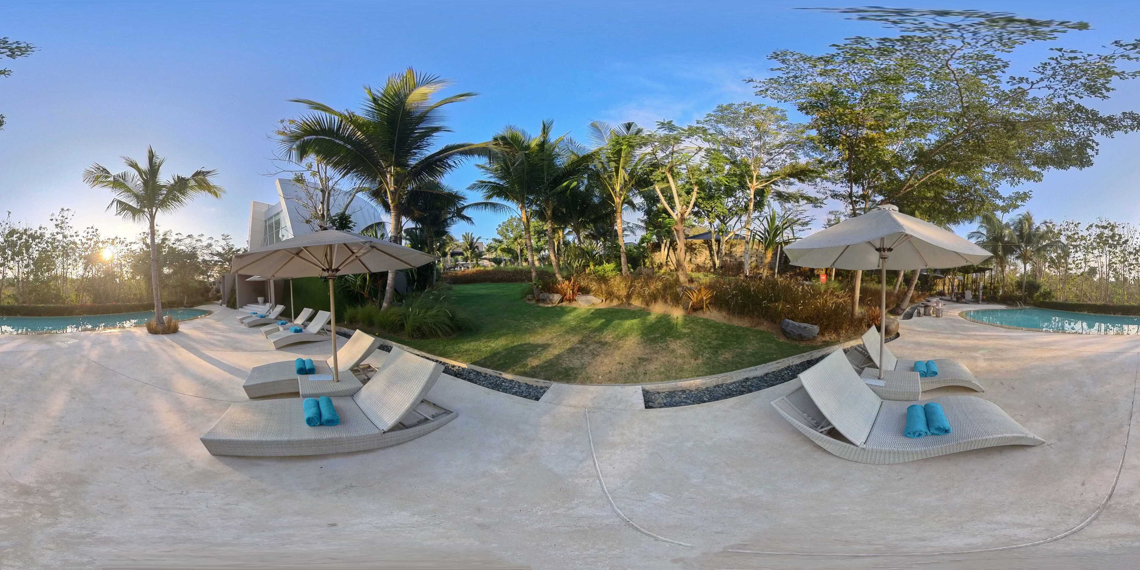 A poolside area with lounge chairs and umbrellas, surrounded by palm trees and a well-maintained lawn.