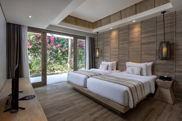 Quarto de hotel moderno com uma cama grande, televisão e vista para flores cor-de-rosa através da porta de vidro.