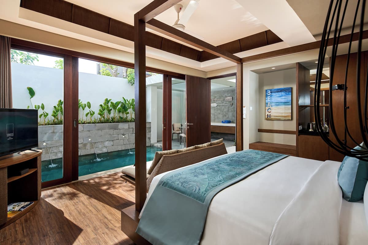 A modern hotel room with a large bed, a TV, a small pool, and a view of the outdoors.