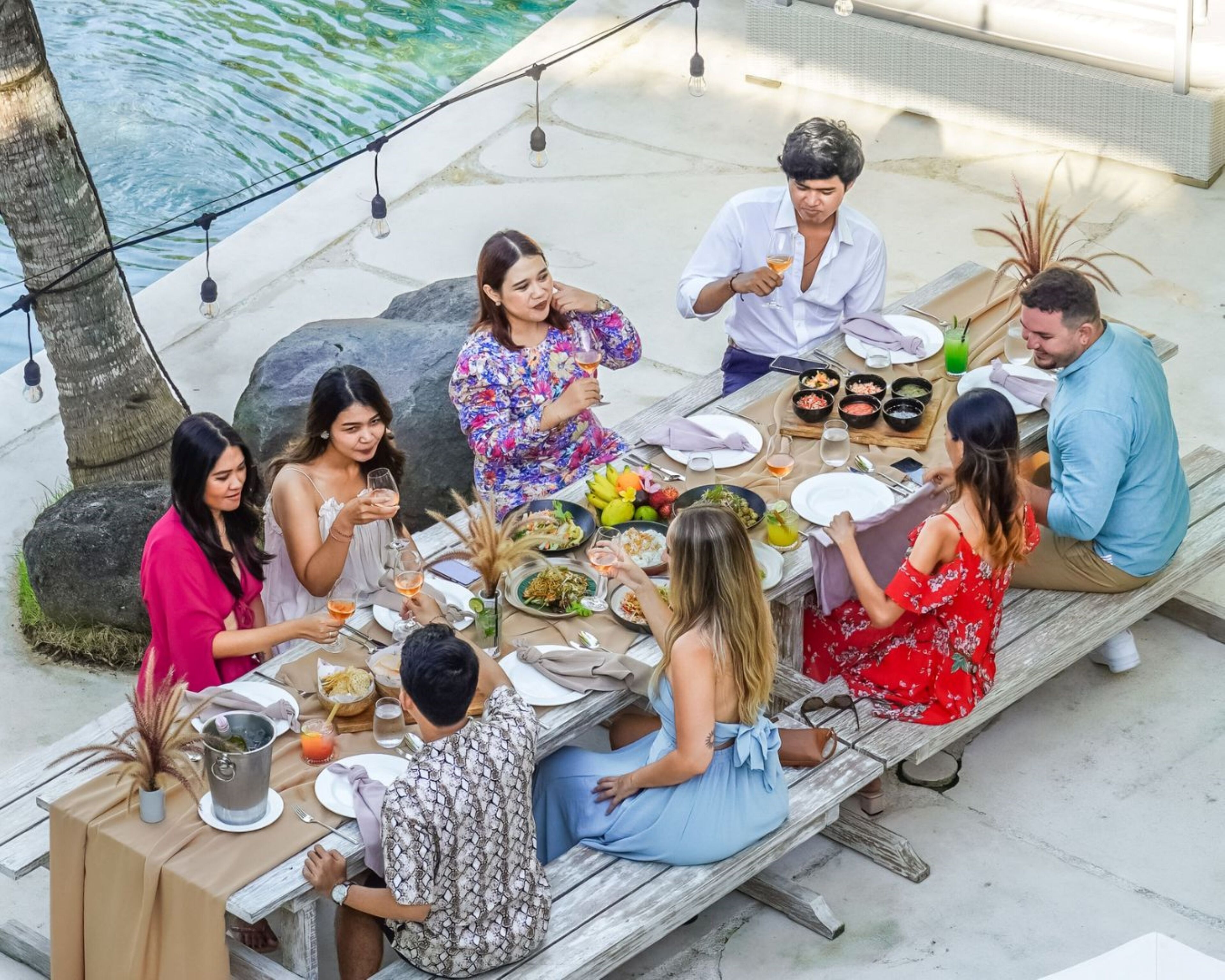 Un grupo de personas cenando al aire libre en una mesa de madera con vistas al agua.