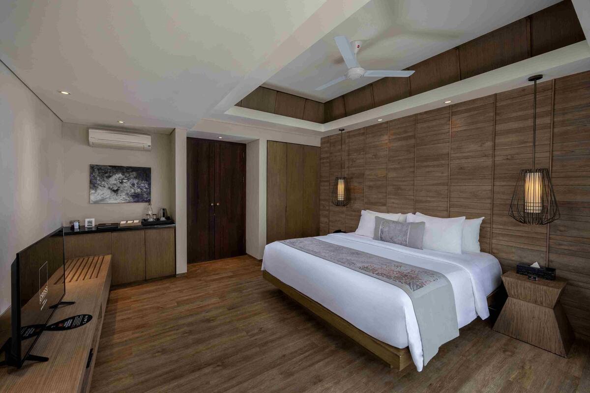 A modern hotel room with a large bed, wooden panel walls, a ceiling fan, and a desk with a chair.