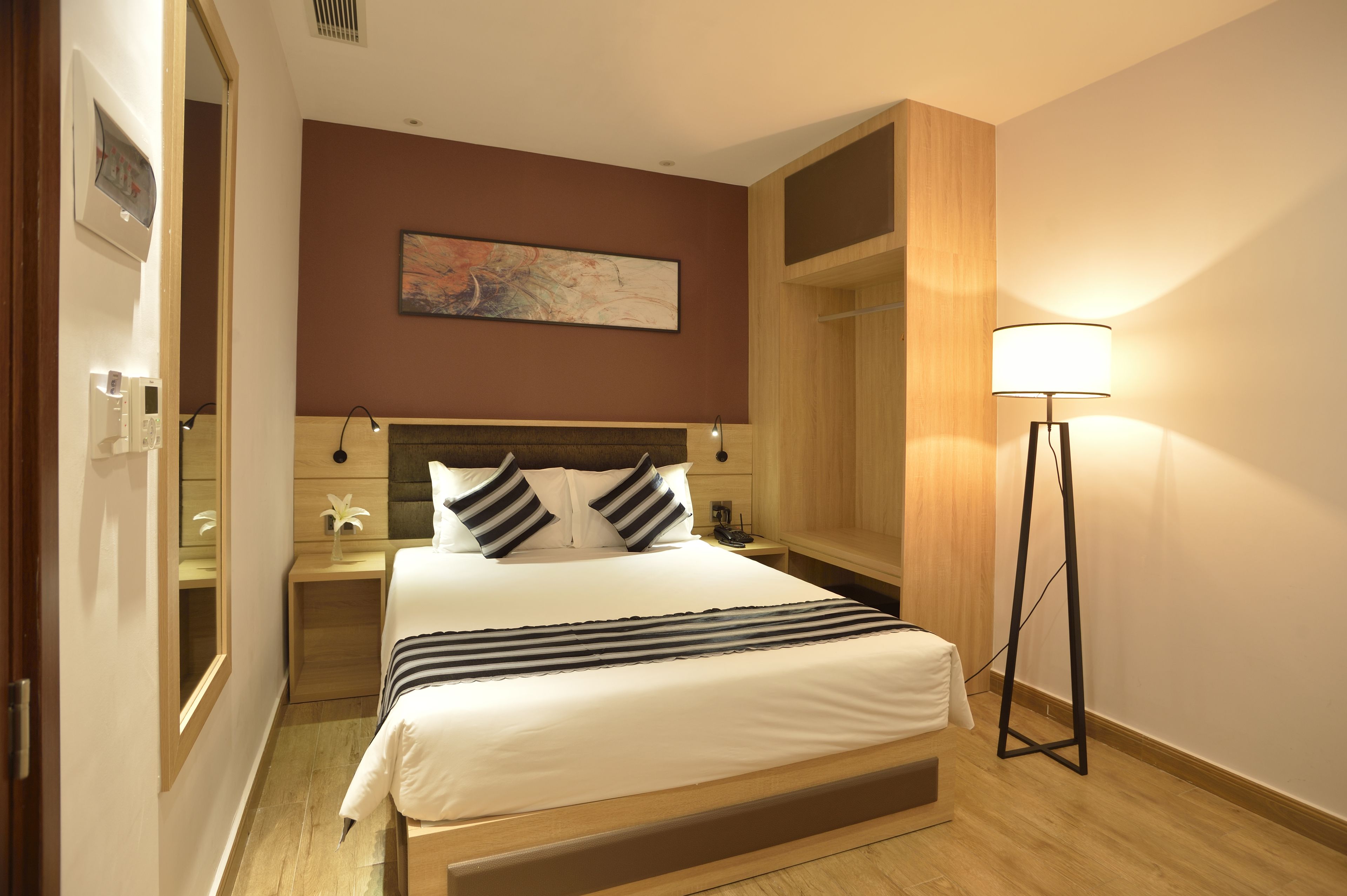 A hotel room with a bed, bedside tables, a lamp, and a painting on the wall.