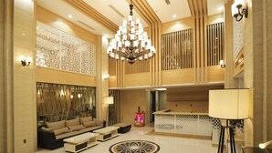 A spacious lobby with a high ceiling, a central chandelier, a seating area with sofas and coffee tables, and a reception desk.